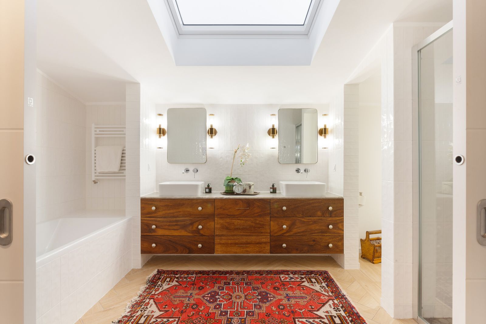 Master bathroom — walnut vanity, skylight, brass sconces and Persian rug